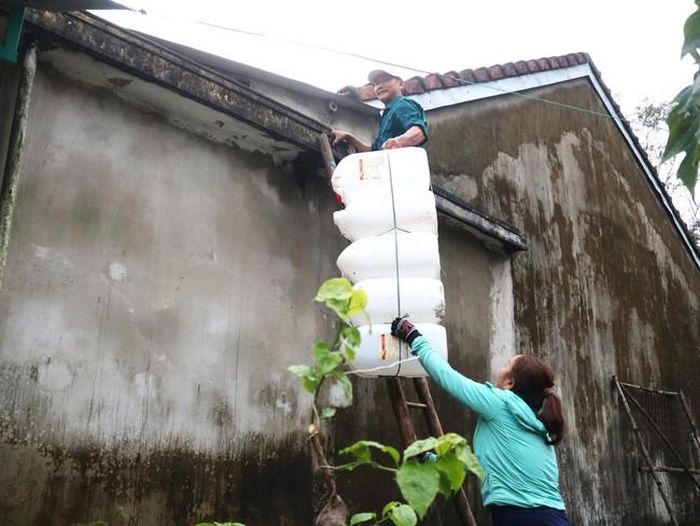 Hai vợ chồng bà Hùng chuẩn bị thùng nước gia cố mái nhà để sẵn sàng ứng phó với mưa bão sắp tới.